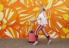 a woman is walking with her luggage in front of an orange flower - patterned wall