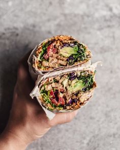 a person holding a wrap filled with meat and veggies on top of a wooden table