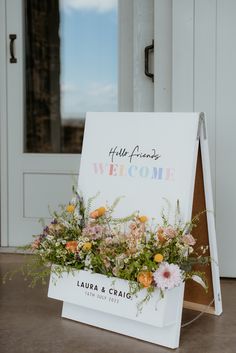 a welcome sign with flowers on it in front of a door