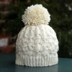 a white knitted hat with a pom - pom on the top sitting on a table