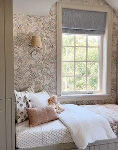 there is a bed with pillows and a teddy bear on it in front of a window