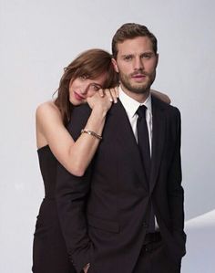 a man and woman posing for a photo in black suits with their arms around each other