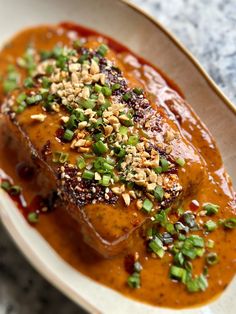 a white plate topped with meat covered in sauce and garnished with green onions