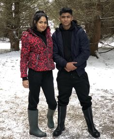 a man and woman standing in the snow wearing rain boots, black pants and red leopard print jacket