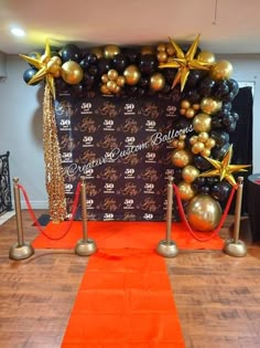 an orange carpet with black and gold balloons