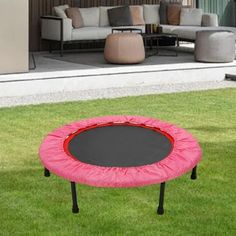 a pink and black trampoline sitting on top of grass next to a couch