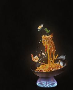 noodles being tossed into a frying pan on top of a gas burner in the dark