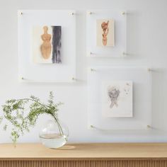 a vase filled with flowers sitting next to three framed pictures on a wall above a wooden table