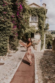 a woman standing on the side of a road in front of a building with vines growing all over it