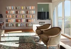 a living room filled with furniture and lots of books on the wall next to a large window