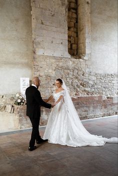 a bride and groom standing in front of a stone wall holding each other's hands