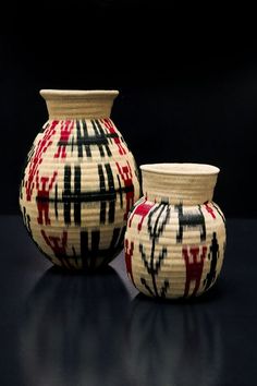 two vases sitting next to each other on a black surface with red and black designs