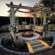 an outdoor fire pit with swings and seating around it at dusk or dawn, surrounded by flowers and greenery