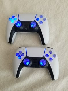 two video game controllers sitting next to each other on a white surface with blue lights