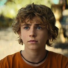 a close up of a young person wearing an orange shirt and looking at the camera