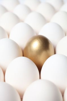 an egg is sitting in the middle of many white eggs with one golden egg on top