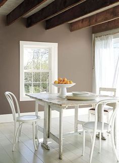 a dining room table with two chairs and a bowl of oranges on the table