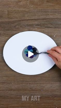 someone is using a spoon to paint a piece of art on a wooden surface with white paper