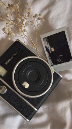 an old camera sitting on top of a bed next to a vase with flowers in it