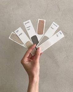 a hand holding five swatches of different shades of paint on a gray background,