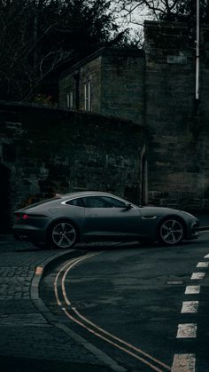 a grey sports car parked on the side of a road next to a brick building