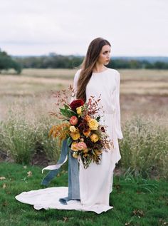 a woman with long hair wearing a white dress and holding a bouquet in her hand