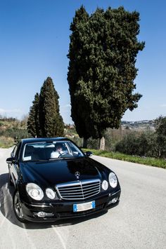 a black car parked on the side of a road with trees in the back ground