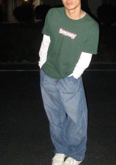 a young man standing in the street at night wearing a green shirt and blue jeans