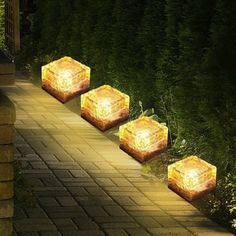 four lights are lit up in the shape of cubes on a brick path at night