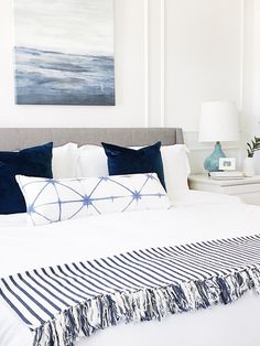 a bed with blue and white pillows on top of it next to a painting in the background