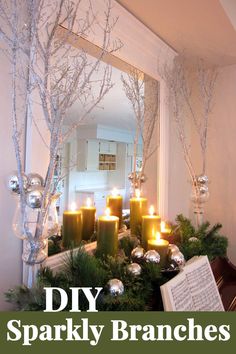 candles are lit in front of a mirror with christmas decorations on the mantle and tree branches