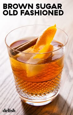 an old fashioned drink in a glass with orange peel and cinnamon on the rim, sitting on a wooden table