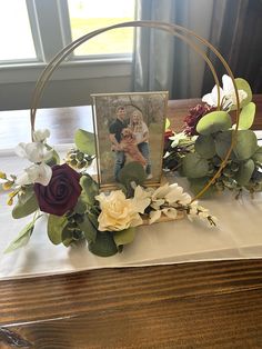 an arrangement of flowers and greenery on a table with a photo in the center