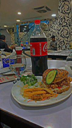 a plate with a sandwich, pickle and chips on it next to a bottle of soda