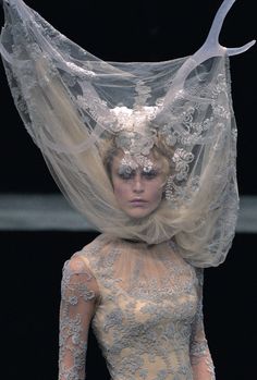 a woman with white hair and veil on her head walking down the catwalk at a fashion show