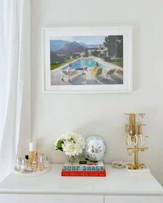 a white dresser with flowers and other items on it in front of a framed photograph