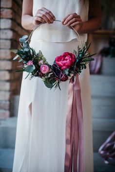 a woman in a white dress holding a pink flower wreath