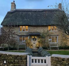 a stone house with a thatched roof and white gate