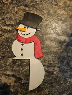 a paper snowman with a red scarf and hat on it's head is standing in front of a granite background