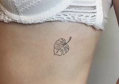 a small tattoo on the side of a woman's stomach that has a leaf in it