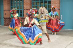 some people are dancing with colorful clothing and headdresses in front of a brick building