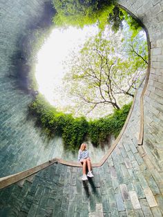 a woman sitting on top of a brick walkway next to a tree filled with leaves