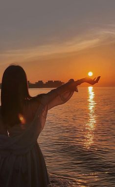 a woman standing in the water with her arms out to the sun setting behind her