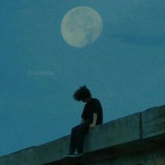 a man sitting on top of a cement wall next to a full moon in the sky