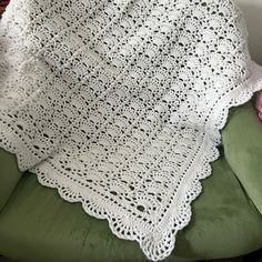 a white crocheted blanket sitting on top of a green chair next to a pink flower