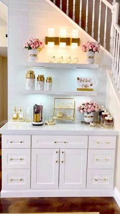 a white counter topped with lots of cupcakes next to a stair case filled with gold and pink flowers