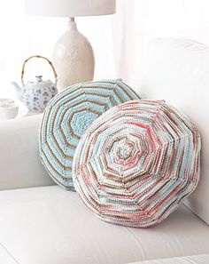 two crocheted pillows sitting on top of a white couch next to a lamp