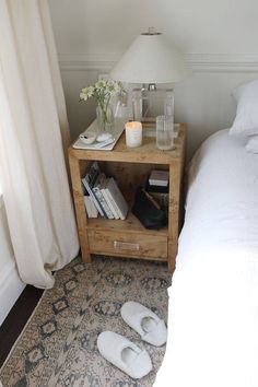 a nightstand with books and candles on it next to a bed