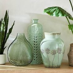 three green vases sitting on top of a wooden table next to a potted plant