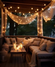 a porch covered in lights and pillows next to a table with a lit candle on it